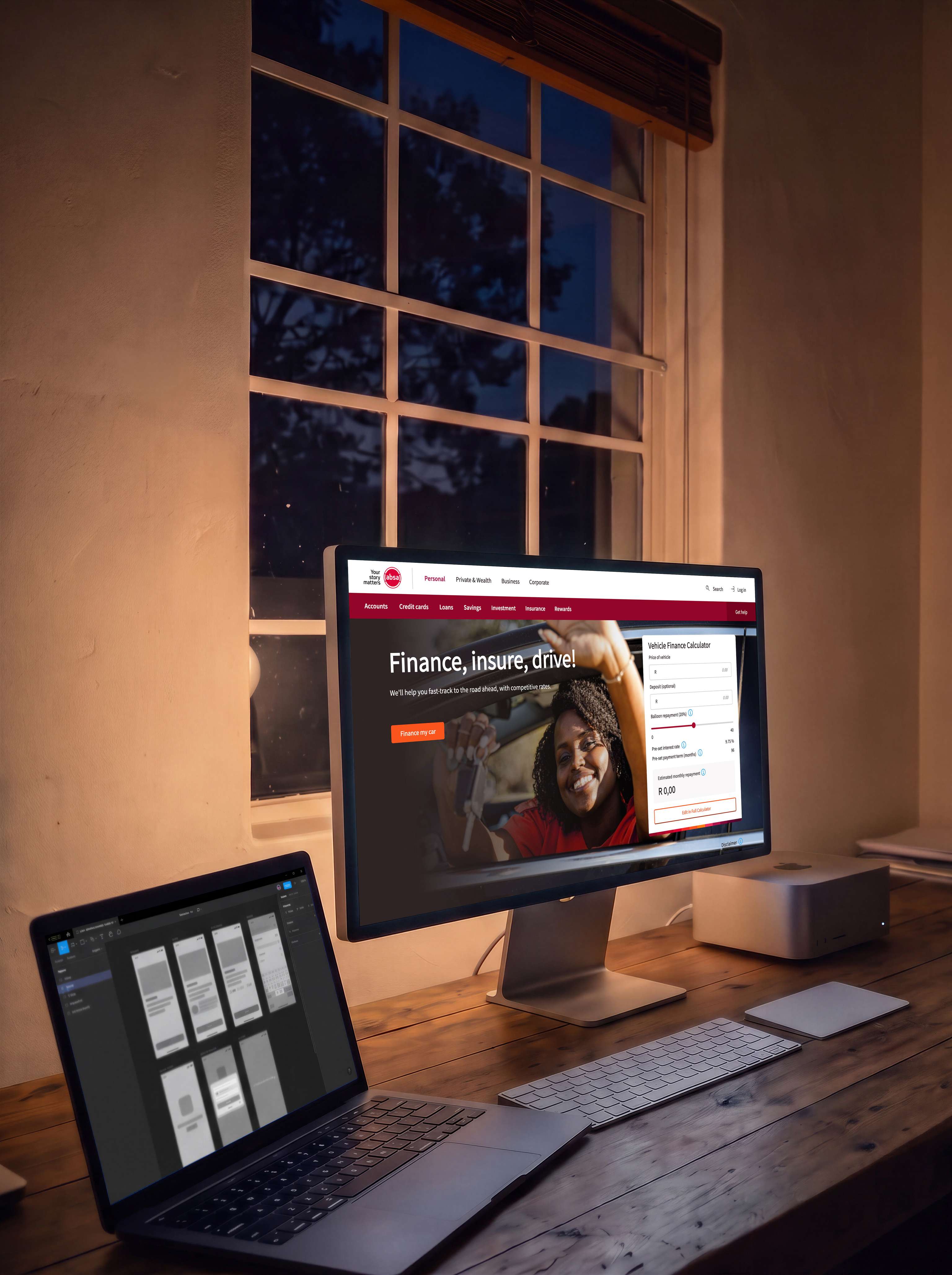 A designer’s desk at dusk lit only by its screens: a large display showing Absa’s vehicle finance page, headed Finance, insure, drive!, with a vehicle finance calculator beside it, and a laptop to the left showing app screens laid out in a design tool.