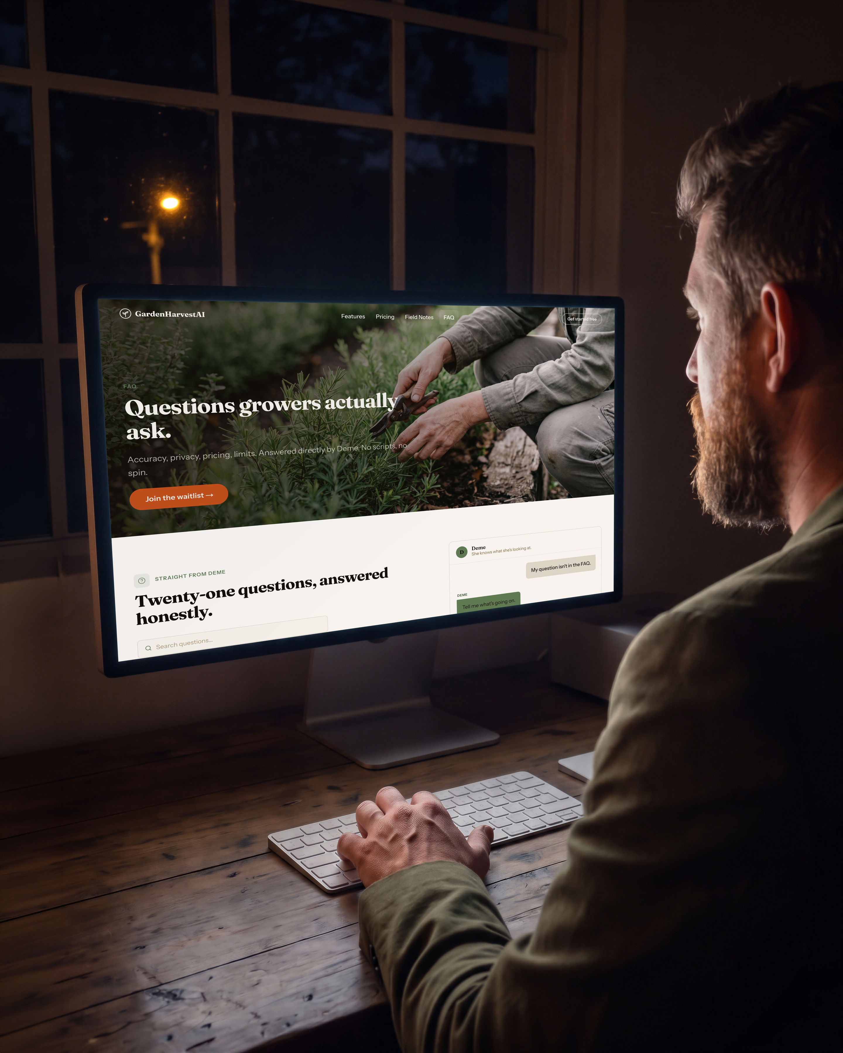 A man seen from behind at a timber desk in a dark room, hands on a keyboard, looking at a large display showing the GardenHarvestAI FAQ page with Deme open in a panel at the right, answering a question that is not in the FAQ.