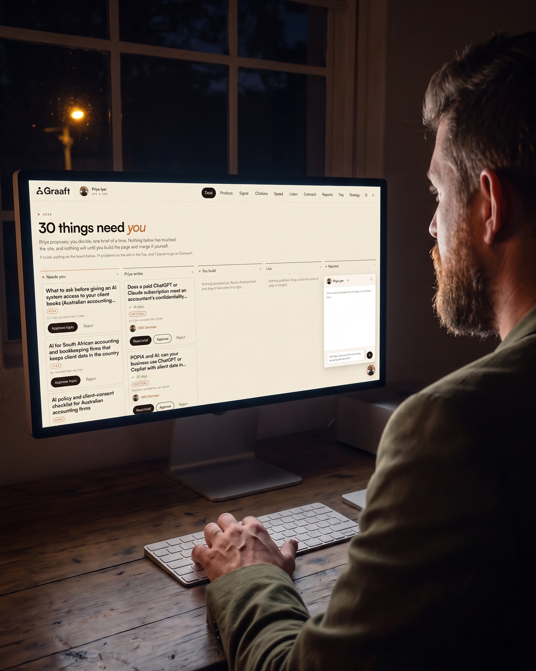 Seen over Will’s shoulder at night: he sits at a timber desk in a dark studio, hand on the keyboard, talking to the Priya console glowing on a large display in front of him.