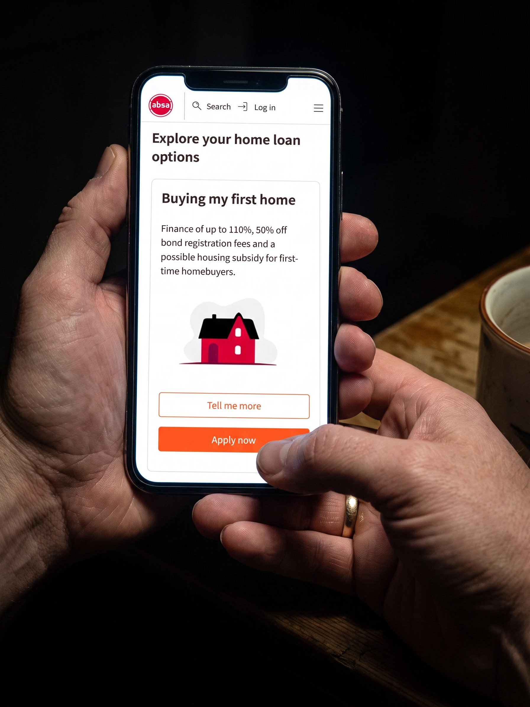 Two hands holding a phone in a dark kitchen, lit only by its screen, which shows Absa's mobile home loans page with an Apply now button.