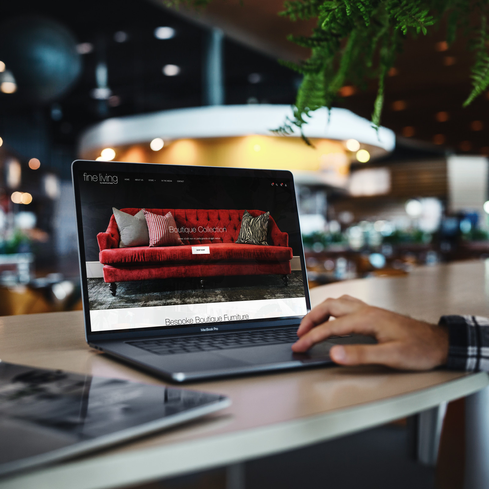 The Fine Living e-commerce site open on a laptop, the Boutique Collection hero showing a red velvet sofa.