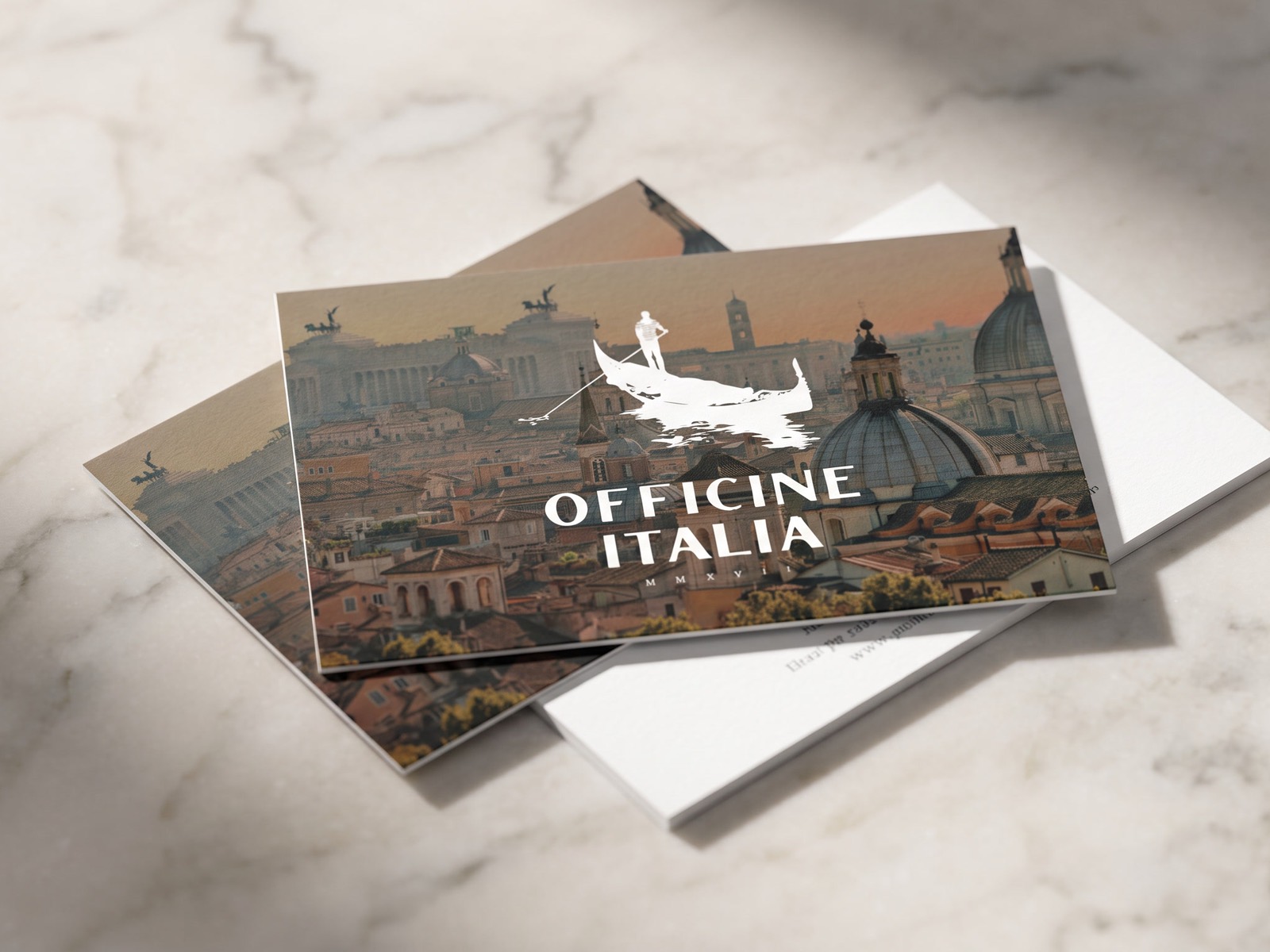 Officine Italia business cards on marble, the mark reversed in white over a photograph of Rome at dusk.