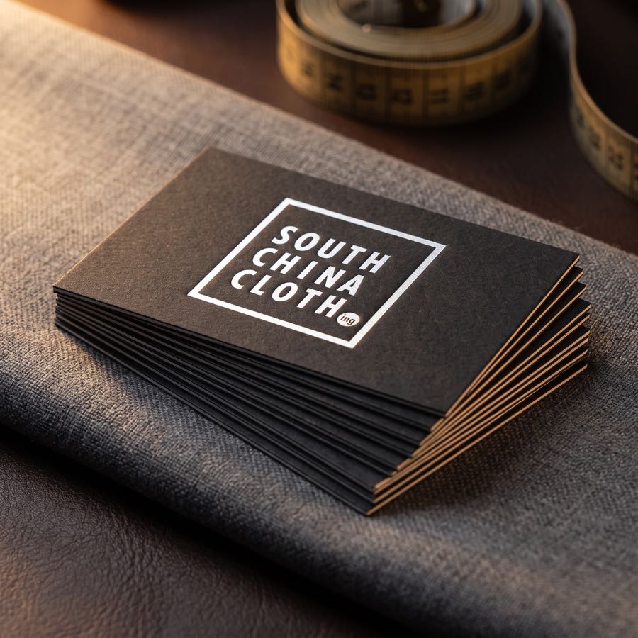 A fanned stack of black South China Clothing business cards, the mark foiled in white, on grey suiting.