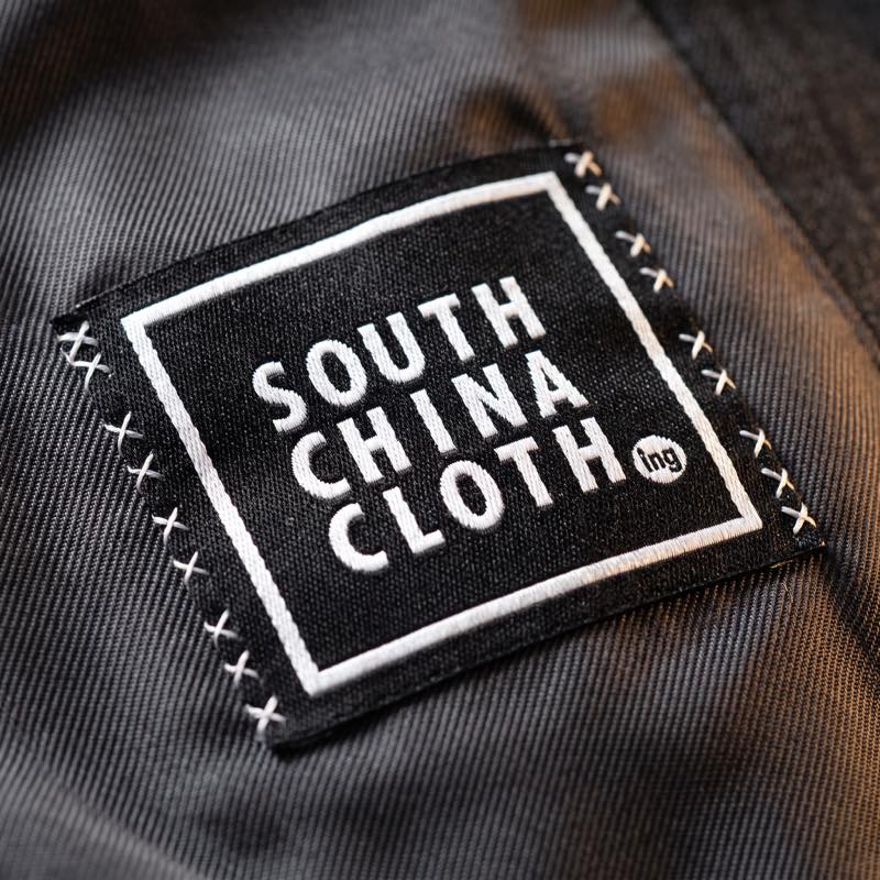 A woven black South China Clothing label cross-stitched into the charcoal lining of a jacket.