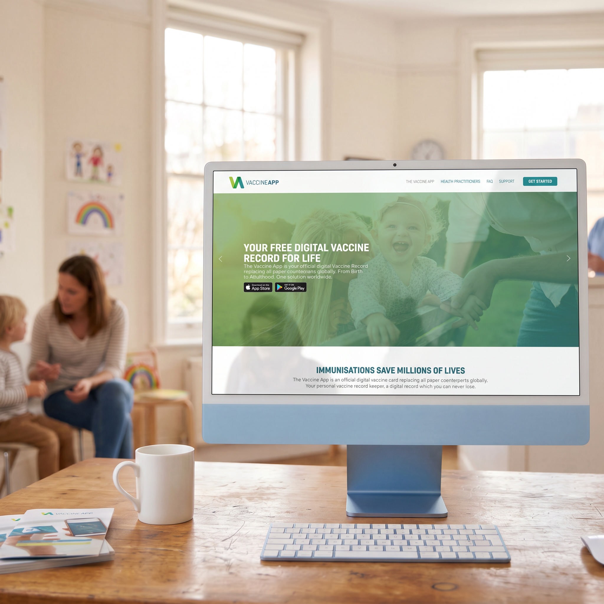 The VaccineApp home page open on a desktop in a paediatric waiting room, a mother and child behind.